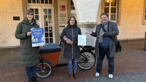 Eine Frau mit Urkunde vor einem Fahrrad. Daneben der Bürgermeister und eine weitere Frau.