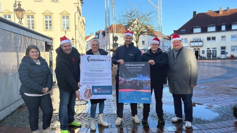 6 Menschen, zwei davon mit Nikolausmützen vor dem Brunnen mit Gerüst