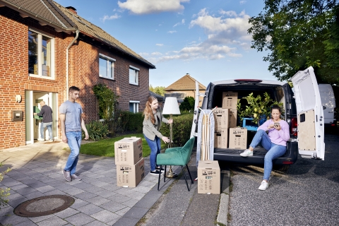 Familie belädt Auto mit Umzugskartons vor Haus