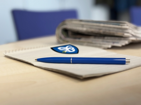 Block mit Stift und Zeitungen verschwommen im Hintergrund