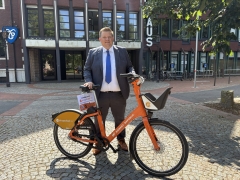 Bürgermeister mit orangem Fahrrad vor Gebäude mit Rathaus-Schriftzug 