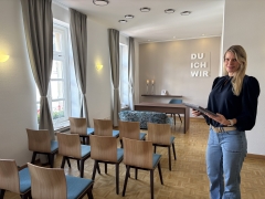 Raum mit Stühlen und einem Tisch sowie einer Frau, die steht