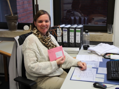 städtische Mitarbeiterin in ihrem Büro mit rotem Umschlag