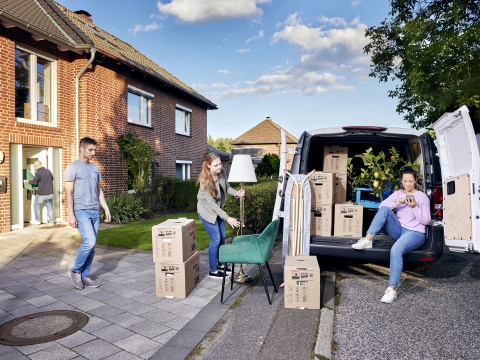 Familie belädt Auto mit Umzugskartons vor Haus