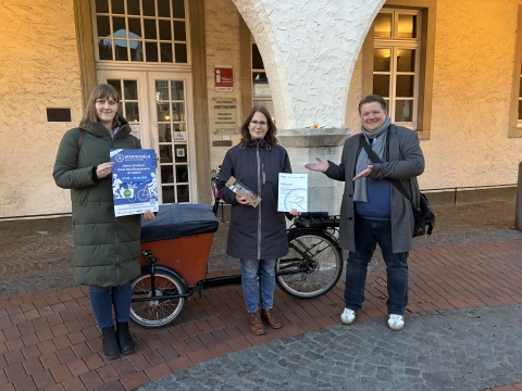 Eine Frau mit Urkunde vor einem Fahrrad. Daneben der Bürgermeister und eine weitere Frau.
