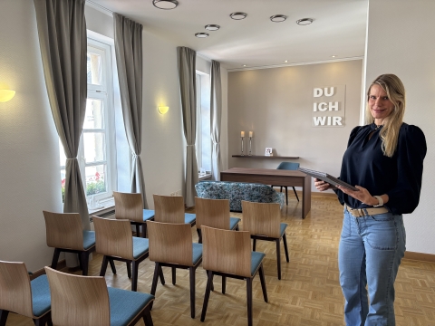 Raum mit Stühlen und einem Tisch sowie einer Frau, die steht